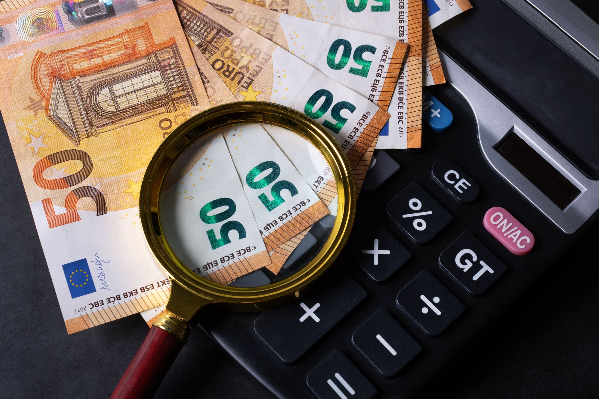 Geld und Taschenrechner liegen unter einer Lupe